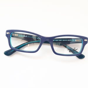 Könnte beinhalten: Blaue rechteckige Brille mit türkisfarbenem Rahmen. Der Markenname "Ray-Ban" ist auf der rechten Linse sichtbar.