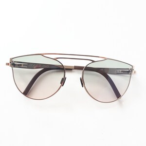 May include: A pair of brown metal sunglasses with a light green gradient lens. The sunglasses have a thin metal frame and a double bridge.
