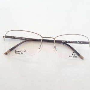 May include: Silver-toned, rimless spectacles with a black temple and the text "Screwless Titanium hinge" on the left lens. The right lens has the text "R RODENSTOCK" on it.