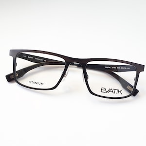 Könnte beinhalten: Schwarze Brille mit Titan-Gestell, auf dem rechten Glas ist der Markenname "EVATIK" aufgedruckt. Das Gestell ist rechteckig mit leicht eckiger Form. Die Bügel der Brille sind mit "BLACK 9163 53B 52□19-145" und "TITANIUM CE" gekennzeichnet.