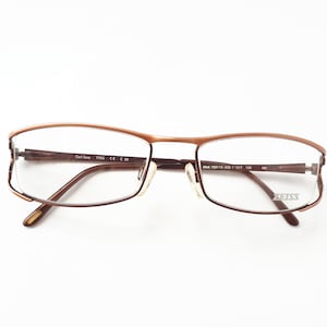 Könnte beinhalten: Eine Brille mit braunem Metallrahmen und klaren Gläsern. Der Markenname "ZEISS" ist auf dem rechten Bügel aufgedruckt. Der linke Bügel trägt den Text "Carl Zeiss" und "FMC CE 29". Der rechte Bügel trägt den Text "Mod. 1521/13 5218 135 017 130 MI".