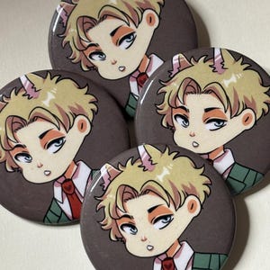 May include: Four round buttons with a cartoon image of a person with blonde hair, wearing a green jacket and red tie. The person has cat ears and a white collar.