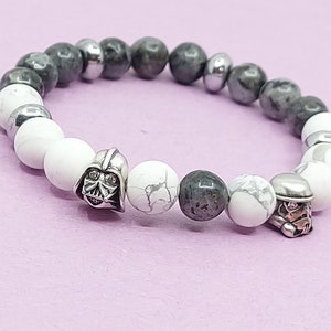 Peut inclure: Un bracelet en perles grises et blanches avec des accents argentés. Le bracelet présente un charme Darth Vader et un charme Stormtrooper.