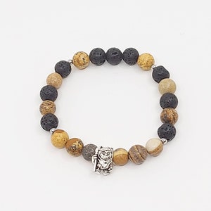 Peut inclure: Un bracelet en perles brunes, noires et blanches avec un charme argenté. Le bracelet est fait de perles de roche volcanique et de jaspe.