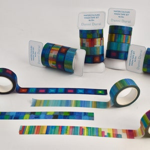 Puede incluir: Conjunto de cuatro cintas washi de acuarela con patrones geométricos azules, verdes, amarillos y rojos. Cada cinta mide 10 metros de largo. Las cintas están empaquetadas en plástico transparente con una etiqueta blanca que dice "Watercolours Washi Tape Set 4x10m Danni Durai".