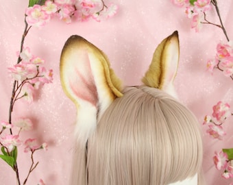May include: A pair of tall, pointed animal ears attached to a headband. The ears feature a gradient of dark brown tips, tan fur, and soft white inner fur with subtle pink shading, positioned atop a light-colored wig with straight bangs.