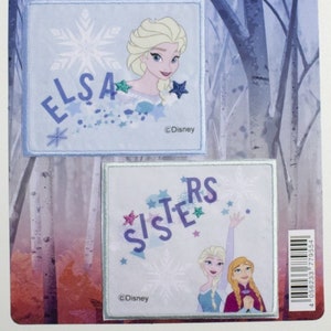 Puede incluir: Parches termoadhesivos de Disney Frozen II. La parte superior del paquete presenta a Anna y Elsa. Se muestran dos parches cuadrados, uno con la imagen de Elsa y la palabra "ELSA", y el otro con la palabra "SISTERS" e imágenes de Elsa y Anna.