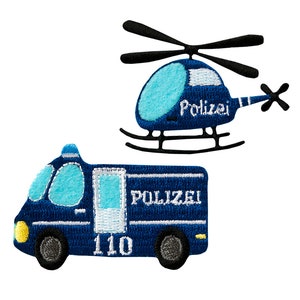 Könnte beinhalten: Zwei blaue Filzpatches, einer mit einem Polizeiauto und einer mit einem Hubschrauber. Das Polizeiauto hat den Schriftzug "POLIZEI" und die Nummer "110" darauf. Der Hubschrauber hat den Schriftzug "Polizei" darauf.