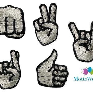 Könnte beinhalten: Fünf gestickte Bügelbilder, die verschiedene Handgesten darstellen: eine Faust, ein Peace-Zeichen, ein Rock'n'Roll-Zeichen, ein Zeigefinger und ein Daumen nach oben. Die Patches sind schwarz mit silbernen Nähten.
