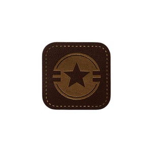 Könnte beinhalten: Ein braunes Lederpatch mit einem genähten Rand. Das Patch zeigt einen braunen Kreis mit einem fünfzackigen Stern in der Mitte. Der Stern ist schwarz und der Kreis hat zwei horizontale Linien.