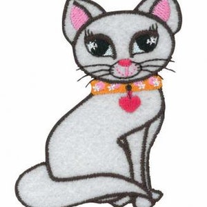May include: White cat with pink ears and a pink heart on a orange collar. The cat is sitting with its tail curled around its body.
