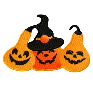Może przedstawiać: Trzy pomarańczowe dynie z twarzami jack-o'-lantern. Środkowa dynia ma na sobie czarny kapelusz czarownicy.