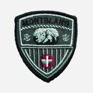 May include: A gray embroidered patch with the words "Mont Blanc" in black lettering. The patch features a white bear in a mountain scene with a red Swiss cross in the center.