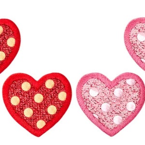Può includere: Tre toppe a forma di cuore con un motivo a pois. Due toppe sono rosse con pois gialli e una toppa è rosa con pois bianchi.