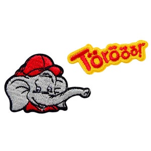 Könnte beinhalten: Zwei gestickte Bügelbilder. Ein Patch zeigt einen Cartoon-Elefanten, der eine rote Baseballkappe und ein rotes Hemd trägt. Der andere Patch ist gelb mit dem Wort "Totoro" in roter Stickerei.