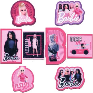 Könnte beinhalten: Ein Set aus neun pinkfarbenen und violetten Aufklebern mit verschiedenen Bildern von Barbie-Puppen. Die Aufkleber zeigen verschiedene Designs, darunter eine Barbie-Puppe in einem rosa Kleid, eine Barbie-Puppe in einer blauen Jacke und eine Barbie-Puppe, die ein rotes Auto fährt. Die Aufkleber zeigen auch den Text "Barbie" und "Boss Mode".