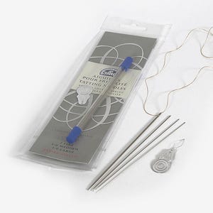 May include: A set of four DMC tatting needles in a clear plastic package with a blue and white label. The label reads "Aiguilles pour Frivole Tatting Needles". The needles are arranged in order of size: fine, medium, and large. The package also includes a small, silver-coloured tatting shuttle.