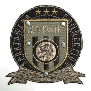 Könnte beinhalten: Gestickter Aufnäher mit einem Schilddesign. Der Aufnäher zeigt das Wort "AUTHENTIC" über einem Löwenemblem mit "EST 1984" auf einem Banner. Der Aufnäher ist in Grün-, Braun- und Goldtönen gehalten, mit den Worten "SPORTS WEAR COLLECTION" am Rand.