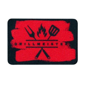 Könnte beinhalten: Rechteckiger schwarzer Aufnäher mit rotem, strukturiertem Hintergrund. Der Aufnäher zeigt eine Grafik von Grillwerkzeugen, einer Flamme und dem Wort "GRILLMEISTER" in weißem Text. Das Design umfasst eine Gabel, einen Pfannenwender und gekreuzte Zangen.