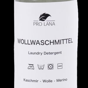 Puede incluir: Una botella transparente de detergente Pro Lana para lana. La etiqueta dice "WOLLWASCHMITTEL Laundry Detergent" con instrucciones de lavado y las palabras "Kaschmir. Wolle. Merino." La botella tiene una tapa blanca.