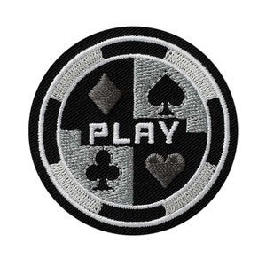 Pode incluir: Etiqueta bordada em preto e branco com um design de ficha de cassino. A ficha tem quatro naipes de cartas de jogo no centro, com a palavra "PLAY" em letras brancas. A ficha é cercada por uma borda branca.