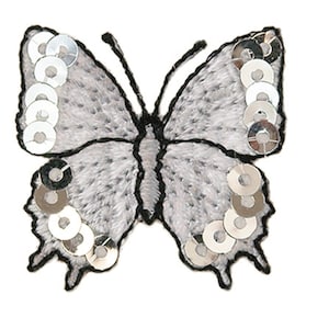Puede incluir: Una aplicación de mariposa bordada en plata y blanco con lentejuelas plateadas. La mariposa tiene un contorno negro y es perfecta para añadir un toque de brillo a las manualidades y la ropa.