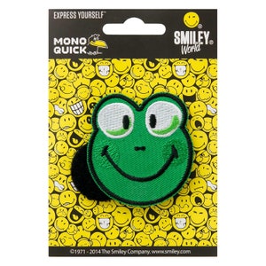 Pode incluir: Etiqueta de ferro com cara sorridente de sapo verde em um cartão branco com borda preta e fundo amarelo com carinhas sorridentes. O cartão diz "Express Yourself" e "Smiley World".