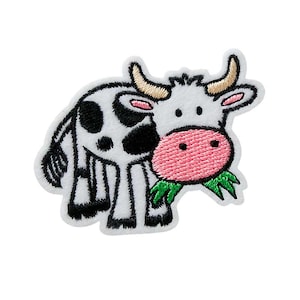 Puede incluir: Parche bordado para planchar de una vaca de dibujos animados con manchas blancas y negras, comiendo hierba verde. La vaca tiene la nariz rosa y los cuernos blancos.