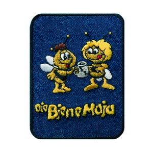 May include: Embroidered patch featuring two cartoon bees holding a mug, set against a blue denim background. The bees are yellow and black with white wings. The text "Die Biene Maja" is embroidered in yellow.
