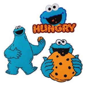 May include: Three embroidered patches featuring the blue Cookie Monster character. One shows the character standing, one shows the character eating a large chocolate chip cookie, and one shows the character above the orange text HUNGRY.