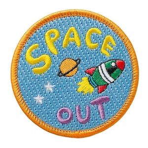 Könnte beinhalten: Ein blauer und orangefarbener gestickter Aufnäher mit den Worten "Space Out" in gelber und violetter Schrift. Ein Cartoon-Raketenschiff und ein Planet sind ebenfalls auf dem Aufnäher gestickt.