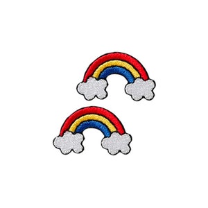 Könnte beinhalten: Zwei gestickte Regenbogen-Patches mit weißen Wolken. Die Regenbögen sind rot, gelb, blau und weiß.