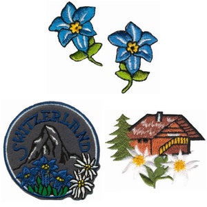 Könnte beinhalten: Vier gestickte Aufnäher mit Schweizer Motiven. Die ersten beiden Aufnäher sind blaue Enzianblumen. Der dritte Aufnäher ist ein runder Aufnäher mit dem Wort "Schweiz" am Rand und einer Bergszene mit blauen Enzian- und Edelweißblumen. Der vierte Aufnäher ist ein braunes Chalet mit einer grünen Tanne und Edelweißblumen.