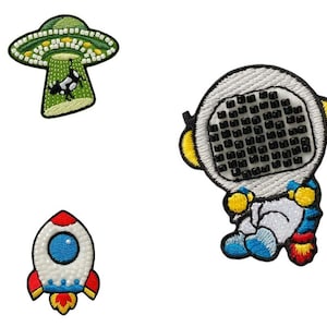 Könnte beinhalten: Drei gestickte Bügelbilder mit einem grünen UFO, einem weißen Astronauten und einer roten und blauen Rakete.