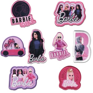 Könnte beinhalten: Acht Bügelbilder mit dem Barbie-Logo und verschiedenen Bildern von Barbie-Puppen. Die Bügelbilder sind in verschiedenen Formen und Größen, darunter ein Kreis, ein Quadrat und ein Rechteck. Die Bügelbilder sind alle mit rosa und weißen Nähten verziert.