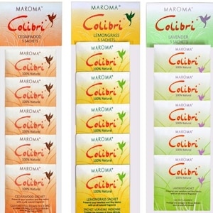 Op de afbeelding: Een display van zes pakken met geurende Colibri-sachets. De sachets zijn verkrijgbaar in drie geuren: cederhout, citroengras en lavendel. Elk pak bevat vijf sachets en is gelabeld met de geur en de merknaam MAROMA. De sachets zijn allemaal wit met een kolibrie-logo en de tekst "Colibri 100% Natuurlijk".
