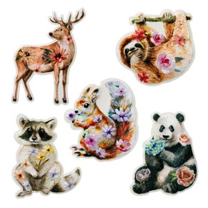 Puede incluir: Cinco parches bordados con diferentes animales con diseños florales. Los animales son un ciervo, un perezoso, una ardilla, un mapache y un panda.