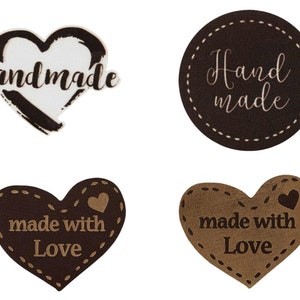 Könnte beinhalten: Vier braune herzförmige Etiketten mit weißen Nähten. Zwei Etiketten sagen "handmade" und "Hand made". Die anderen beiden Etiketten sagen "made with Love".