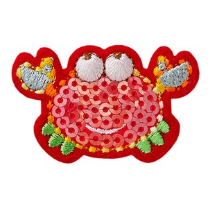 May include: Red embroidered crab applique with sequins. The crab has large eyes and a smiling mouth.