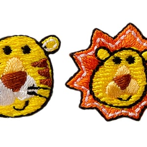 May include: Two embroidered patches depicting cartoon animal faces. One is a yellow tiger with brown stripes, a white muzzle, and black eyes. The other is a yellow lion with an orange starburst mane and a white stitched border.