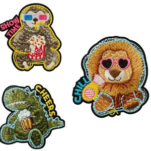 Könnte beinhalten: Drei gestickte Bügelbilder mit einem Faultier, das eine 3D-Brille trägt und Popcorn hält, mit dem Text "Show Time", einem Löwen, der eine herzförmige Sonnenbrille trägt und ein gelbes Getränk hält, mit dem Text "Chill", und einem grünen Dinosaurier, der ein Bier hält, mit dem Text "Cheers".