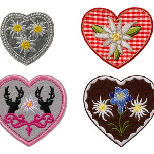 Könnte beinhalten: Vier gestickte Filz-Herz-Patches. Einer ist grau mit weißen Edelweiß-Blumen, einer ist rot-weiß kariert mit einer weißen Edelweiß-Blume, einer ist grau mit rosa Besatz und zwei schwarzen Hirschen und einer ist braun mit weißen Edelweiß-Blumen und einer blauen Enzian-Blume.