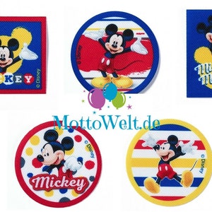 May include: Five colourful iron-on patches featuring Mickey Mouse in different poses. The patches are round and square with red, yellow, blue, and white backgrounds. The patches have the text "Mickey" and "Mickey Mouse" on them.
