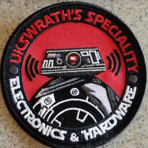 May include: A black and white embroidered patch with red accents. The patch features a robot with a radio antenna and the text "U.S.WRATH'S SPECIALTY ELECTRONICS & HARDWARE".