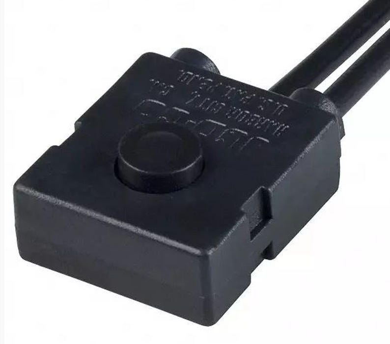 May include: A black electrical component with a round button on top and two black wires extending from the top. The component has text on the side. The item is likely used in electronics or appliances.