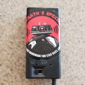 May include: Black rectangular device with a red and black graphic of a Star Wars droid and the text "KRATH'S SPECIAL HARDWARE FOR STAR WARS AMPS". The device has an on/off switch and a cord.