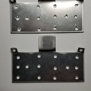 May include: Two silver metal plates with multiple holes and a tab on the top. The plates are identical.