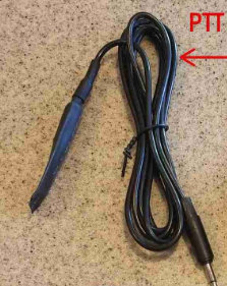 May include: Black push-to-talk (PTT) cable with a coiled design. The cable has a black connector on one end and a black PTT button on the other. The text "PTT" is visible in red.