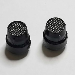 Può includere: Due filtri di aspirazione dell'aria in plastica nera con una griglia in metallo. I filtri sono rotondi e hanno un diametro di circa 2,5 cm.