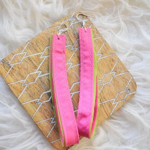 May include: A pair of long, pink and green fabric earrings. The earrings are made of multiple layers of fabric, sewn together. The fabric is a soft, silky material.